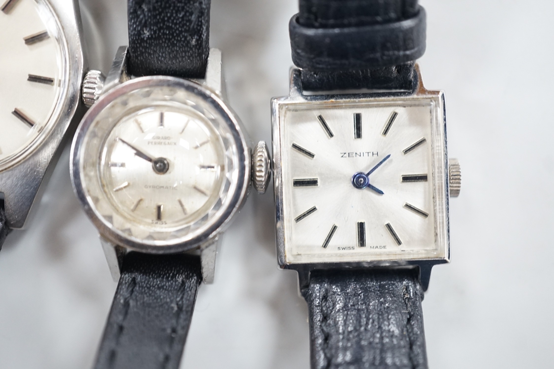 A lady's stainless steel Omega manual wind wrist watch, with baton numerals, together with a lady's stainless steel Zenith square dial manual wind wrist watch and a similar Girard Perregaux manual wind wrist watch.